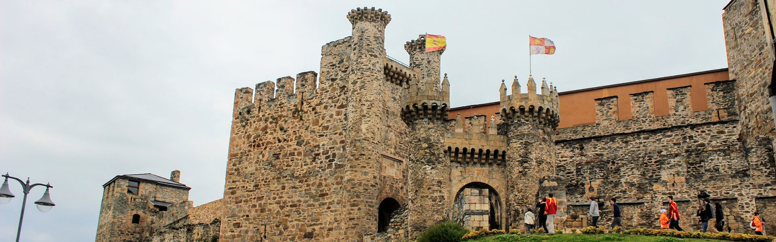 The front of a stone castle, with people walking in an out.